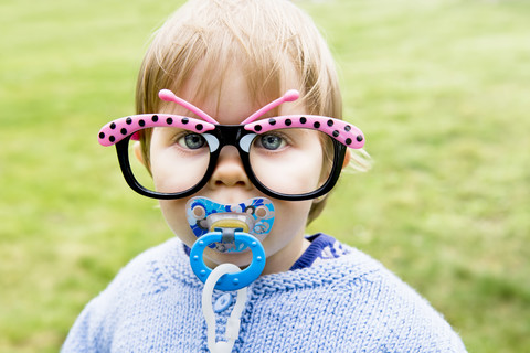 Porträt eines kleinen Mädchens mit Schnuller und lustiger Schmetterlingsbrille, lizenzfreies Stockfoto