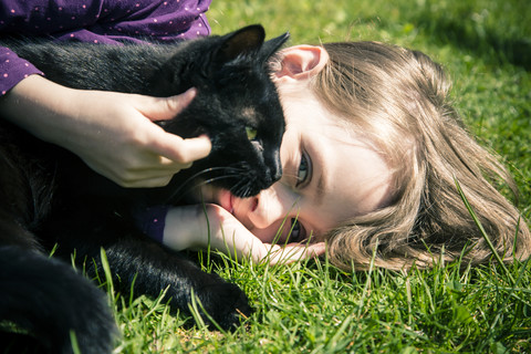 Mädchen liegend auf einer Wiese mit schwarzer Katze, lizenzfreies Stockfoto