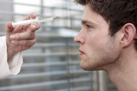 Arzt hält Spritze ins Gesicht eines jungen Mannes, lizenzfreies Stockfoto