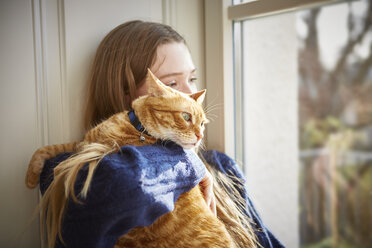 Weiblicher Teenager mit Katze schaut durch das Fenster - DISF002028