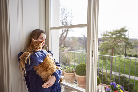 Weiblicher Teenager mit Katze schaut durch das Fenster, lizenzfreies Stockfoto