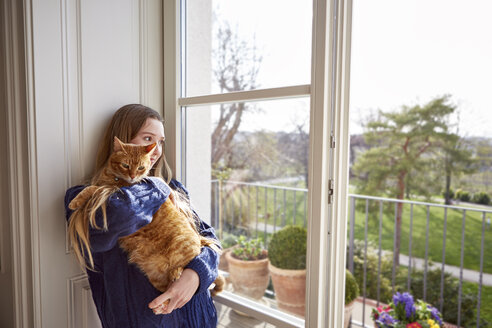 Female teenager with cat looking through window - DISF002029