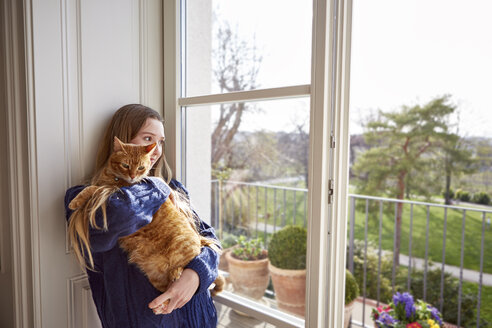 Weiblicher Teenager mit Katze schaut durch das Fenster - DISF002029