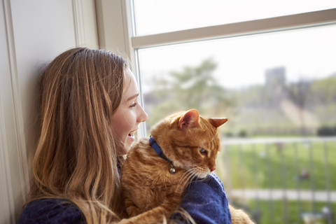 Female teenager with cat looking through window stock photo