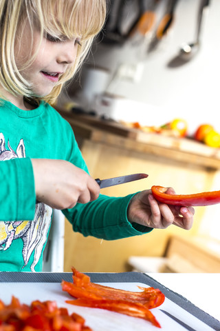 Kleines Mädchen schneidet rote Paprika, lizenzfreies Stockfoto
