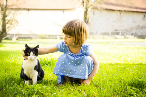 Kleines Mädchen streichelt Katze auf einer Wiese, lizenzfreies Stockfoto