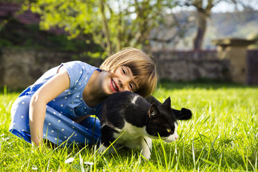 Porträt eines lächelnden kleinen Mädchens mit Katze auf einer Wiese - LVF003202
