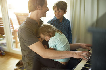 Father playing piano with daughter on his lap, son watching - MAO000053