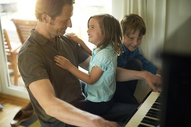 Father playing piano with daughter on his lap, son watching - MAO000054