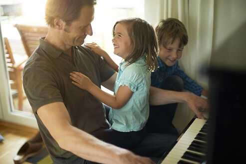 Vater spielt Klavier mit Tochter auf seinem Schoß, Sohn schaut zu - MAO000054