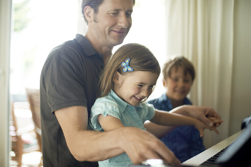 Father playing piano with daughter on his lap, son watching - MAO000038