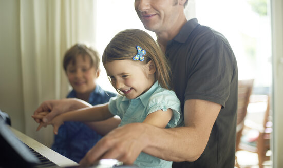 Father playing piano with daughter on his lap, son watching - MAO000039