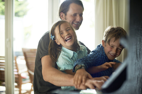 Father playing piano with daughter on his lap, son watching - MAO000040