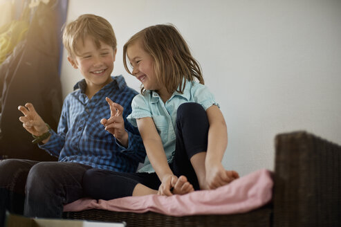 Brother and sister sitting on bench at home, having fun - MAO000044