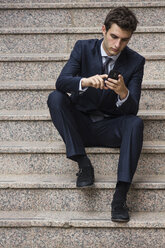 Porträt eines jungen Geschäftsmannes, der auf einer Treppe sitzt und ein Smartphone benutzt - ABZF000005