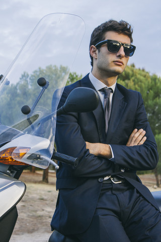 Portrait of young businessman wearimg sunglasses sitting on motor scooter stock photo