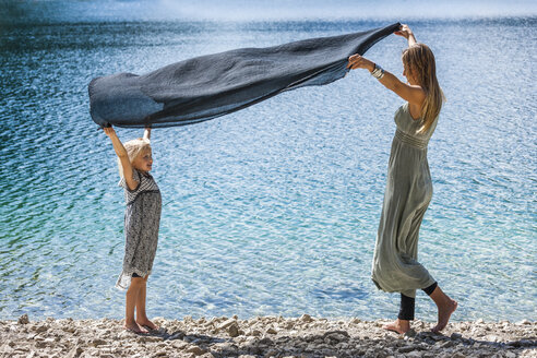 Austria, Tyrol, Lake Plansee, mother and daughter holding cloth at lakeshore - TCF004629