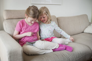 Two sisters with digital tablet on couch - PAF001317
