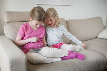 Zwei Schwestern mit digitalem Tablet auf der Couch - PAF001317