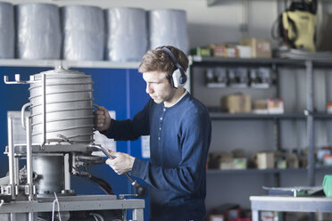 Technician in workshop lifting lid of a machine - SGF001543