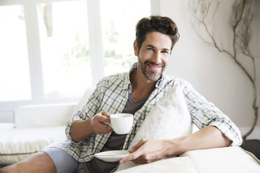 Mature man sitting on sofa, drinking coffee - TOYF000013