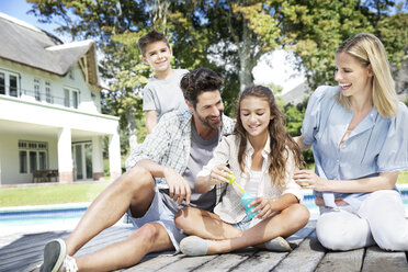 Glückliche Familie am Pool beim Spielen mit Seifenblasen - TOYF000036