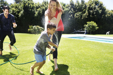 Glückliche Familie, die mit dem Gartenschlauch Wasser spritzt - TOYF000057