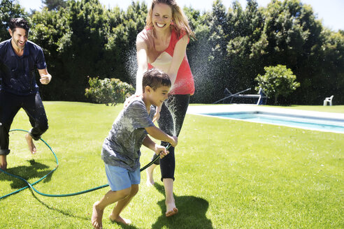Glückliche Familie, die mit dem Gartenschlauch Wasser spritzt - TOYF000057