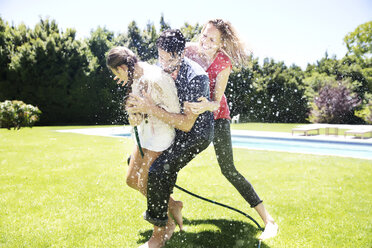 Glückliche Familie, die mit dem Gartenschlauch Wasser spritzt - TOYF000059