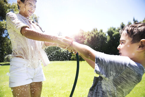 Bruder und Schwester spritzen Wasser mit dem Gartenschlauch - TOYF000061