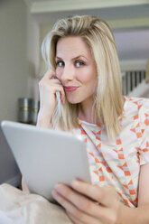 Blonde Frau sitzt auf dem Sofa und benutzt ein digitales Tablet - TOYF000096