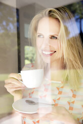 Blonde Frau steht am Fenster und trinkt Kaffee - TOYF000099
