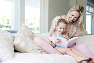 Mother and daughter sitting on sofa, reading book - TOYF000102