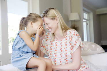 Mother and daughter sitting on sofa, giggling - TOYF000105