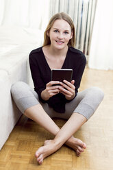 Portrait of woman sitting on the floor with mini tablet - DAWF000354