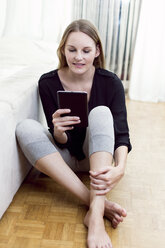 Porträt einer Frau, die auf dem Boden sitzt und ein Mini-Tablet benutzt - DAWF000351