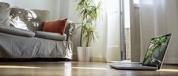 Laptop standing on wooden floor in a living room - RIBF000050