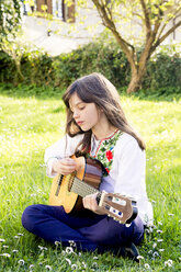 Girl sitting on a meadow playing guitar - LVF003224