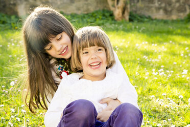 Two sisters sitting together on a meadow in the garden - LVF003234