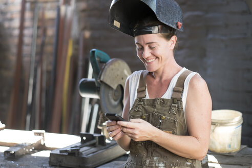 Female welder in metal workshop using mobile phone - ABAF001668