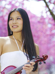 Portrait of young woman with viola in front of blossoming cherry tree - MADF000193