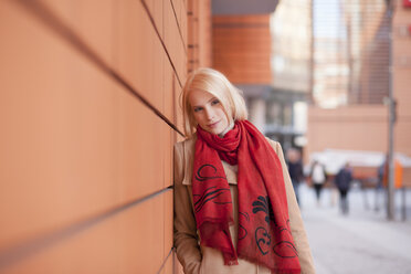 Porträt einer jungen Frau mit rotem Schal, die an der Wand lehnt - MMFF000831