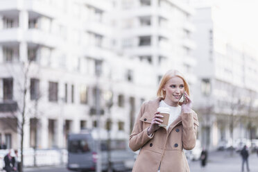 Germany, Berlin, young woman with coffee to go telephoning with smartphone - MMFF000842