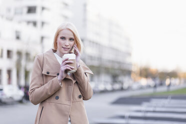 Deutschland, Berlin, junge Frau mit Kaffee zum Telefonieren mit Smartphone - MMFF000843