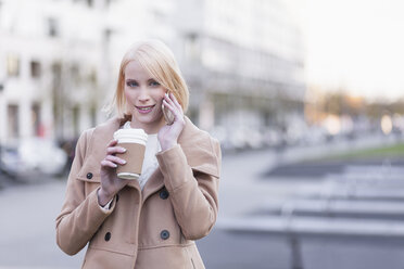 Deutschland, Berlin, junge Frau mit Kaffee zum Telefonieren mit Smartphone - MMFF000844