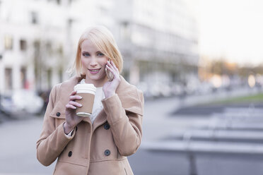 Germany, Berlin, young woman with coffee to go telephoning with smartphone - MMFF000844