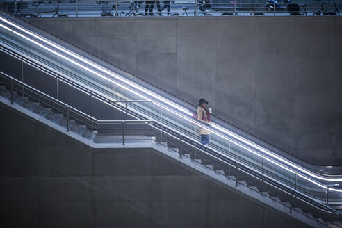 Junge Frau mit Kaffee zum Mitnehmen auf der Rolltreppe stehend - MMFF000840