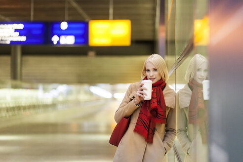 Junge Frau mit Kaffee zum Mitnehmen wartet in einem Bahnhofsgebäude - MMFF000841