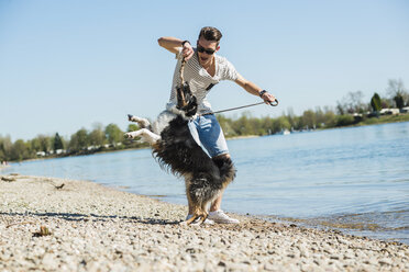 Deutschland, Mannheim, junger Mann spielt mit Hund am Flussufer - UUF003929