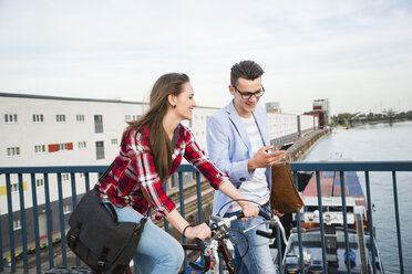 Germany, Mannheim, young man and woman with bicycle and cell phone on bridge - UUF003913